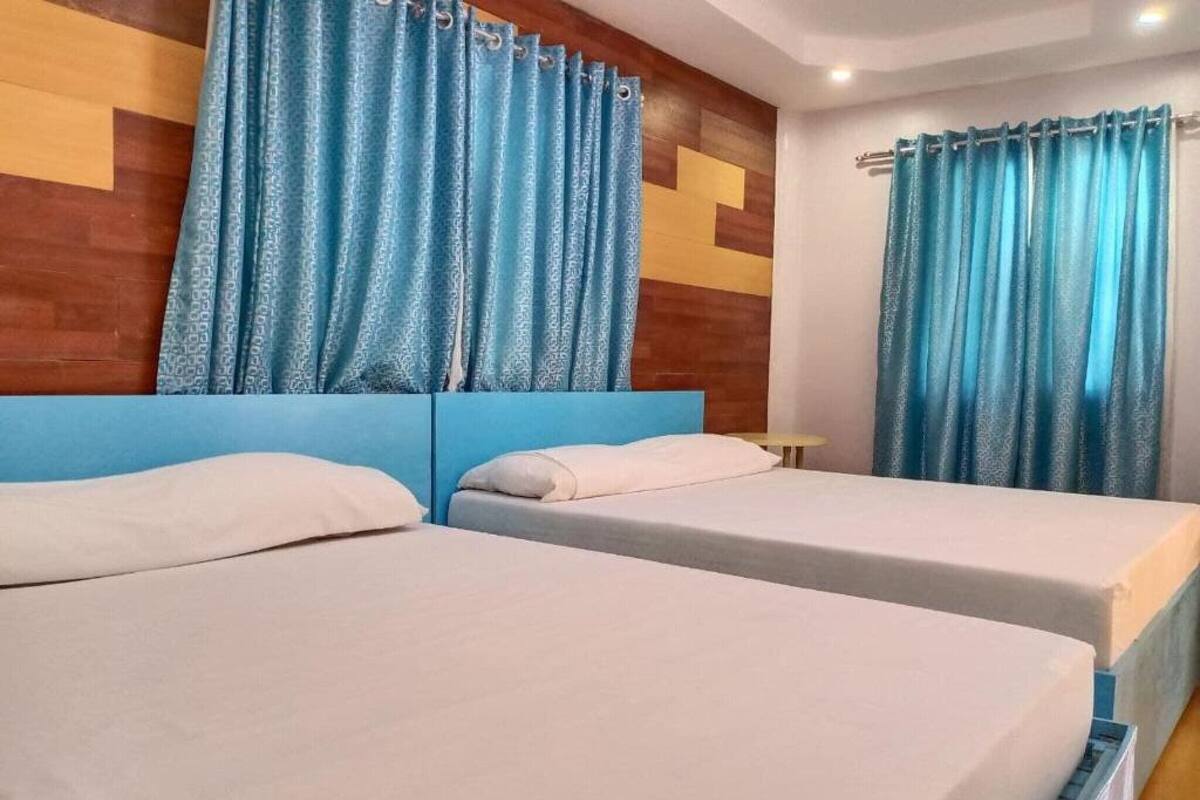 A hotel room with two beds, blue curtains, and a wooden headboard.