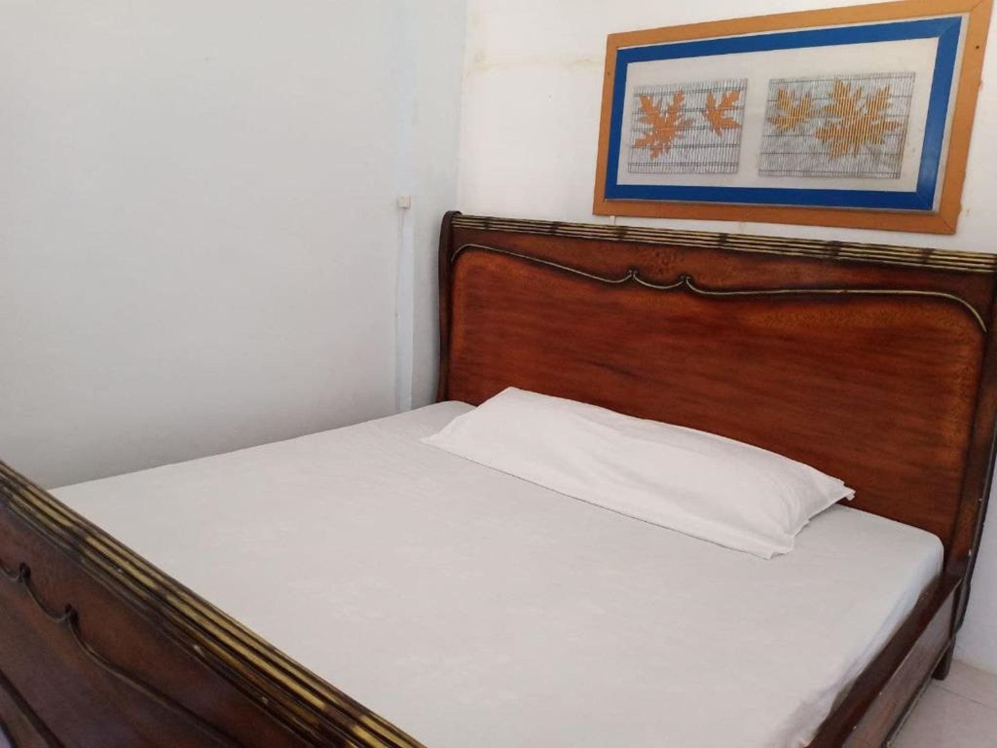 A single bed with a wooden headboard and white bedding in a room with plain walls.