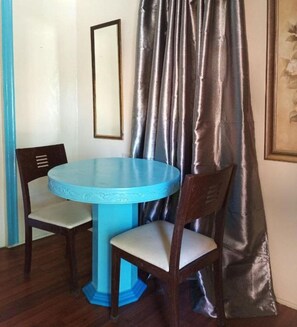A room with a round table and two chairs, a blue base, a wooden chair with a cushion, a framed picture on the wall, and a curtain. - Reddoorz Near Gaisano Grand Cordova (Cordova)