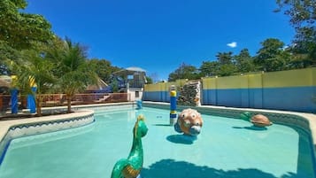 A swimming pool with a dolphin statue, a water slide, and a stone wall.