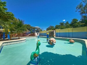 Une piscine ornée d’une statue de dauphin, avec un toboggan et un mur en pierre.