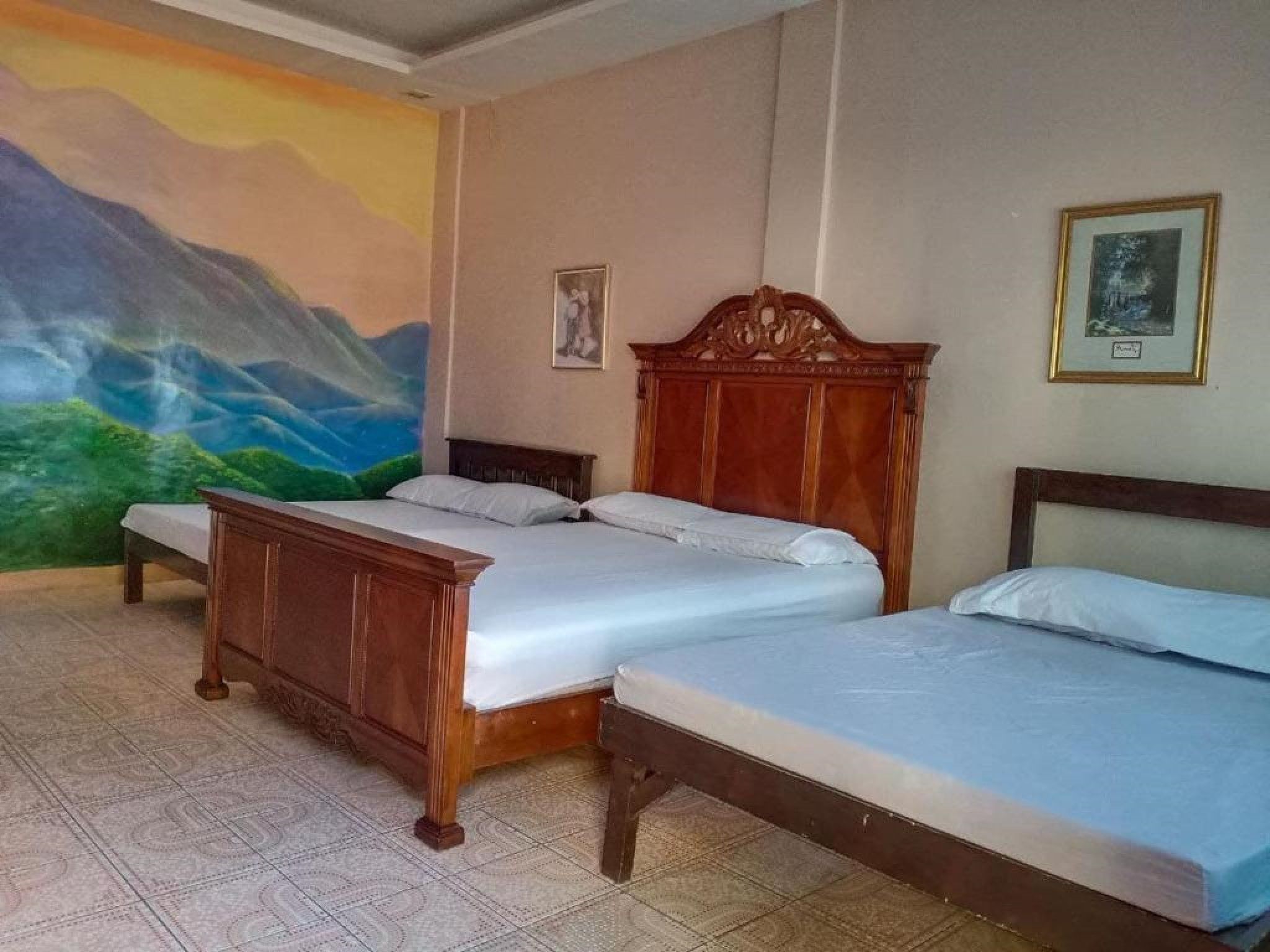 Una camera d'albergo con due letti, un affresco sulla parete e un quadro incorniciato.
