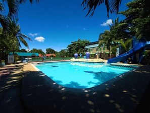 Une piscine avec un toboggan bleu, entourée de palmiers et d’un bâtiment doté d’un toit végétalisé.