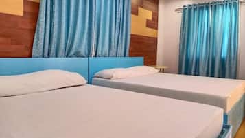 Ein Hotelzimmer mit zwei Einzelbetten, einem hölzernen Kopfteil und blauen Vorhängen.