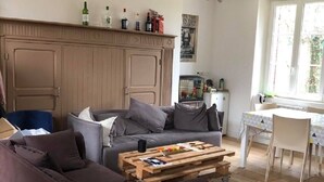 Ein gemütliches Wohnzimmer mit einem dunkelbraunen Sofa, einem Holztisch und einem Essbereich mit weißem Tisch und Stühlen.