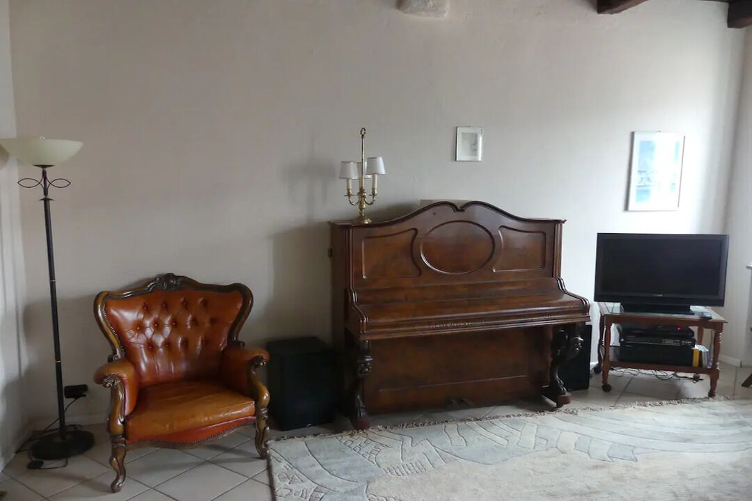 Un salon avec un piano en bois, un fauteuil en cuir, une lampe sur pied et un téléviseur.
