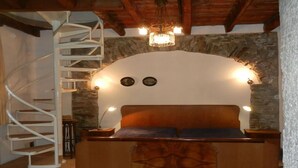 A bedroom with a wooden bed, a spiral staircase, and a stone wall. - Fewo für 6 Personen "200 Jahre Altes Pfarrhaus" (Ghiffa)