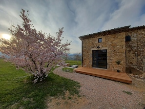 A stone building with a wooden deck and a cherry blossom tree in front. - Gîte de Charme au Coeur de L'ardèche Verte (Saint-Barthélémy-le-Plain)