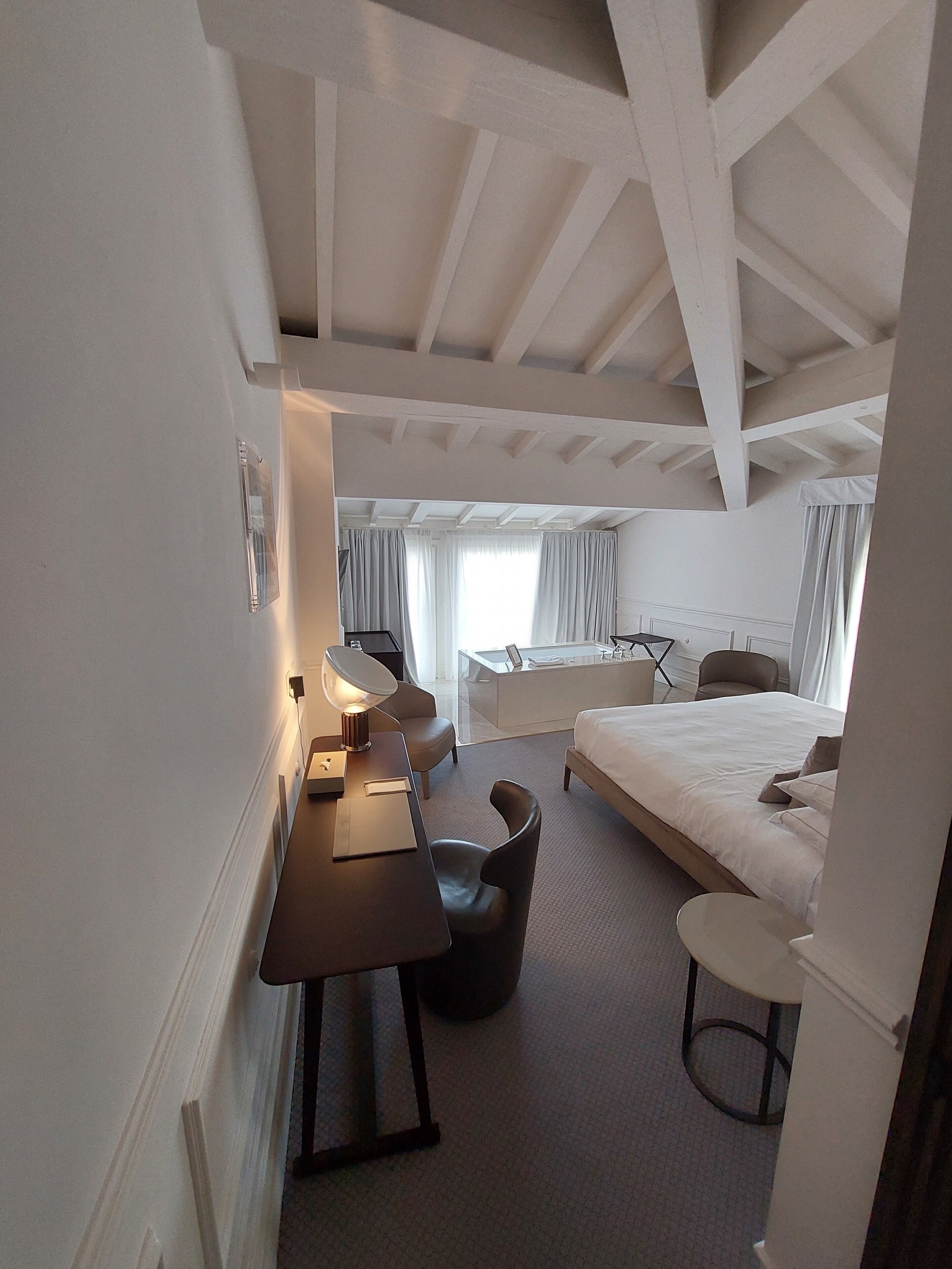 Una camera d'albergo moderna con un letto grande, una scrivania con una lampada, una sedia e un tavolino rotondo.