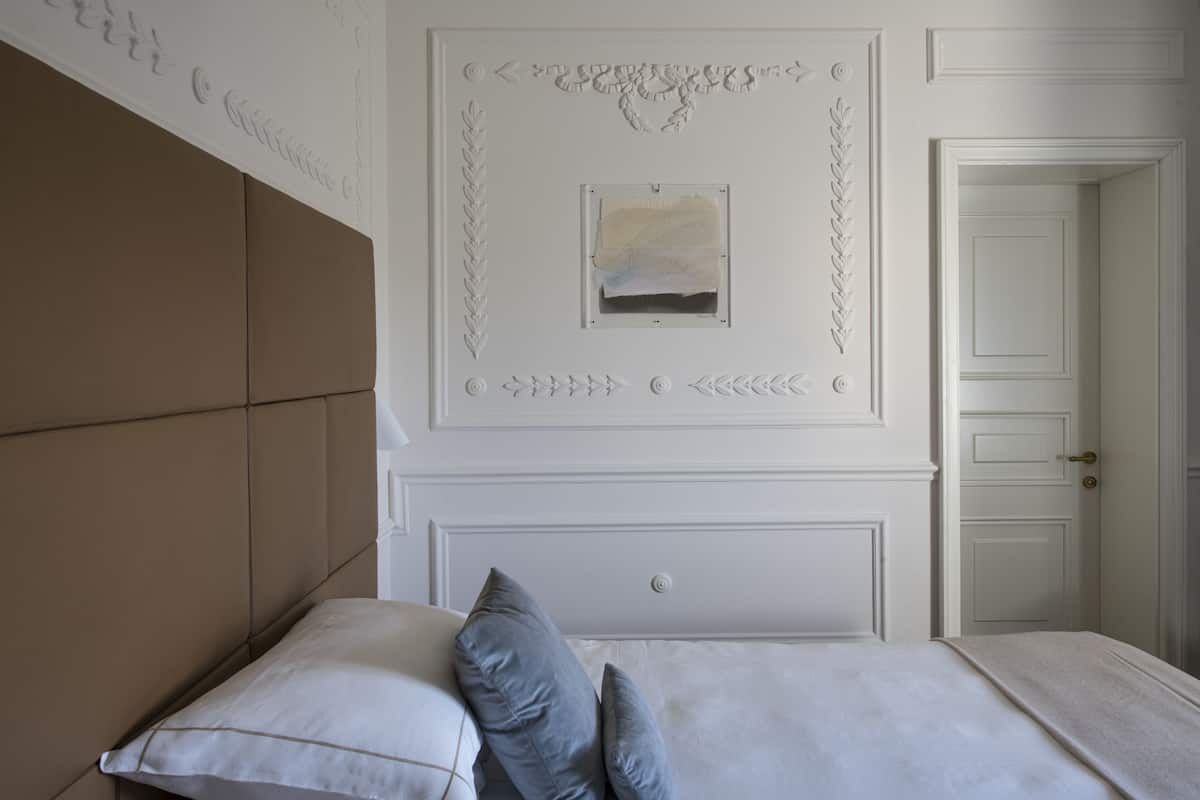 A bedroom with a large bed, a headboard, a framed picture on the wall, and a door to the right.