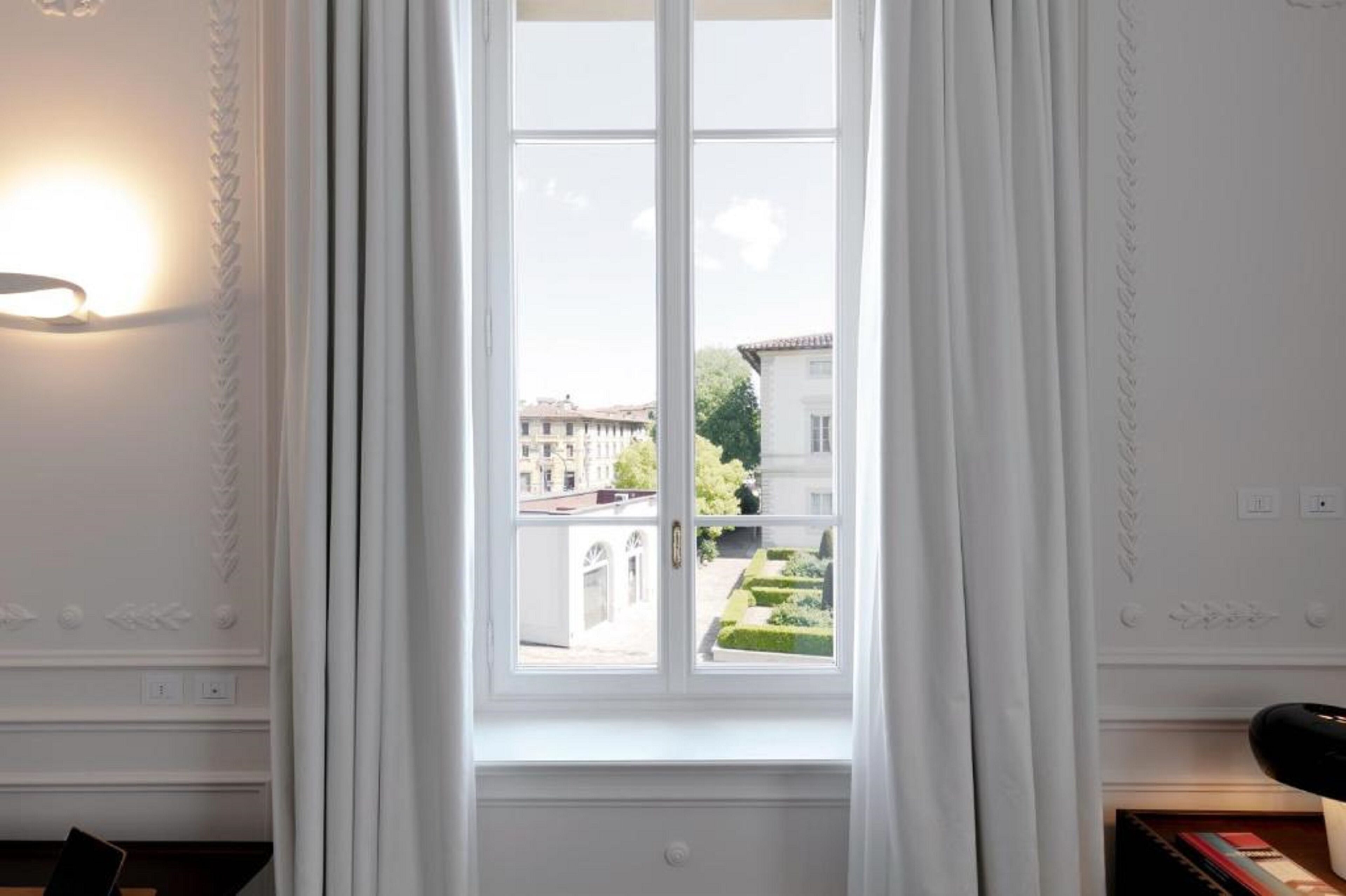 A room with a large window, white curtains, and a wall-mounted light fixture.