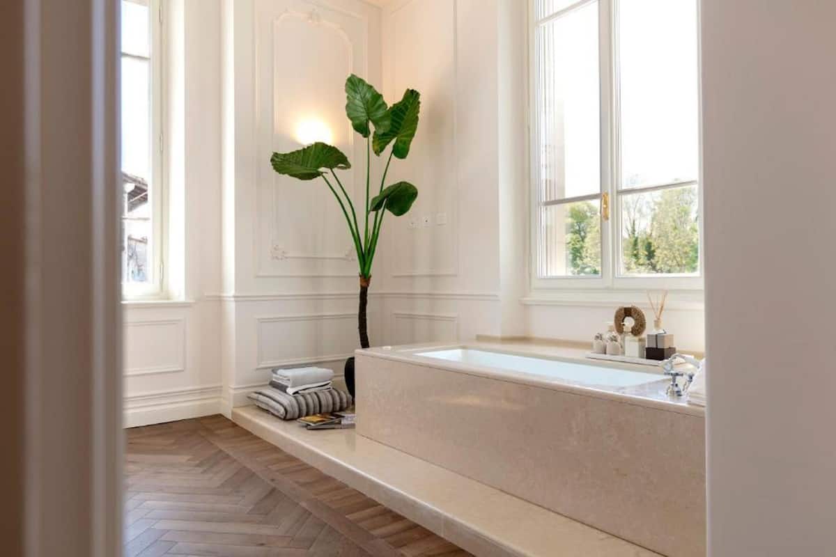 A modern bathroom with a large bathtub, a potted plant, and a window providing natural light.