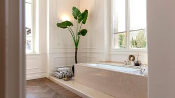 Un baño moderno con una bañera grande, una planta en maceta y un ventanal que deja entrar luz natural.
