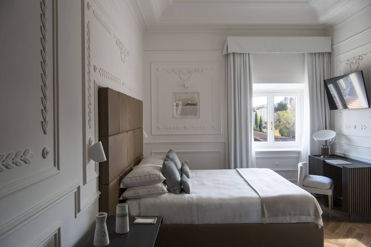 A modern hotel room with a large bed, a desk, and a view of the outdoors.