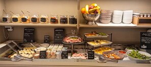 Un bufé con diversos alimentos y acompañamientos, incluyendo queso, frutas y carnes.