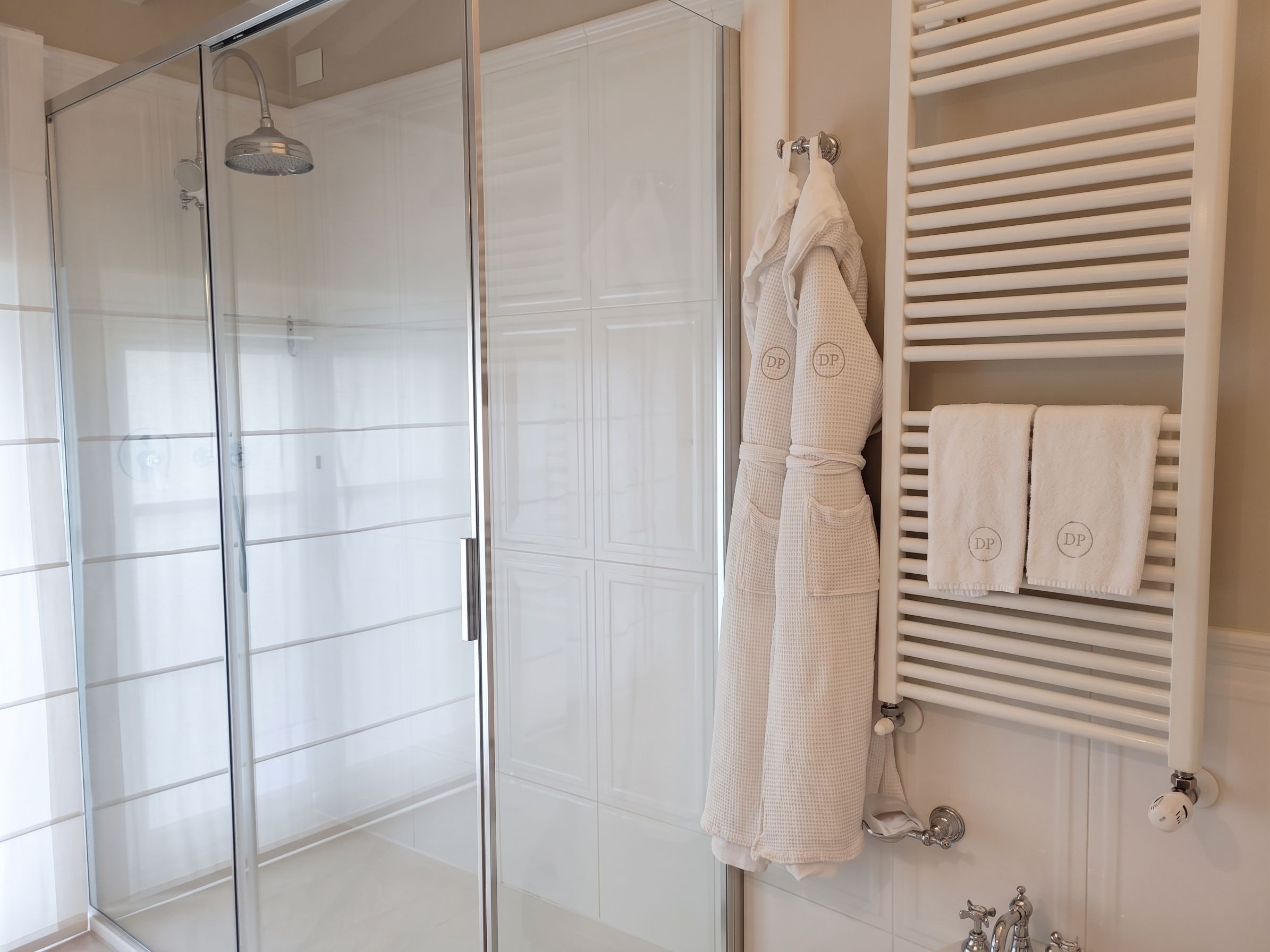 A bathroom with a glass shower enclosure, a towel rack with white towels, and a white tiled wall.