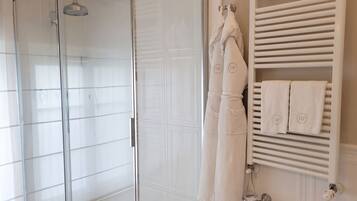 A bathroom with a glass shower enclosure, a towel rack with white towels, and a white tiled wall.