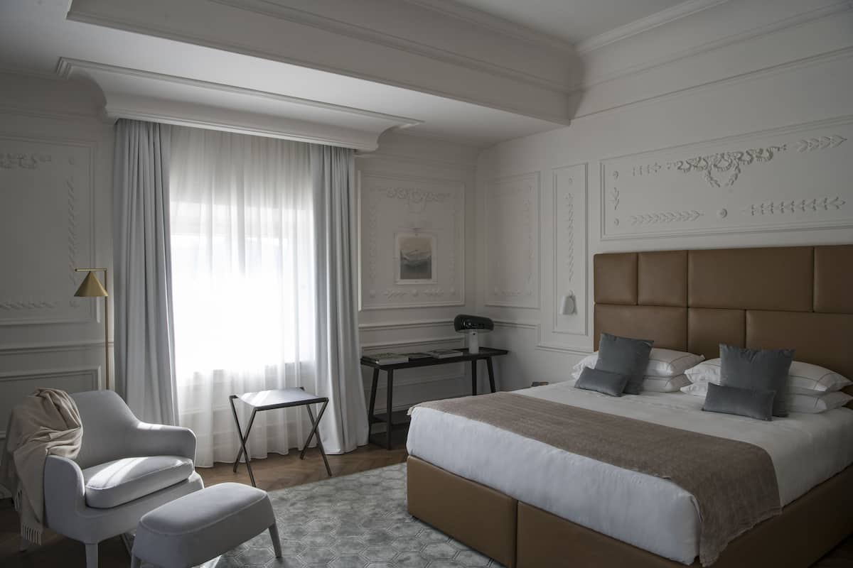 A hotel room with a large bed, a chair, a desk, and a window with curtains.