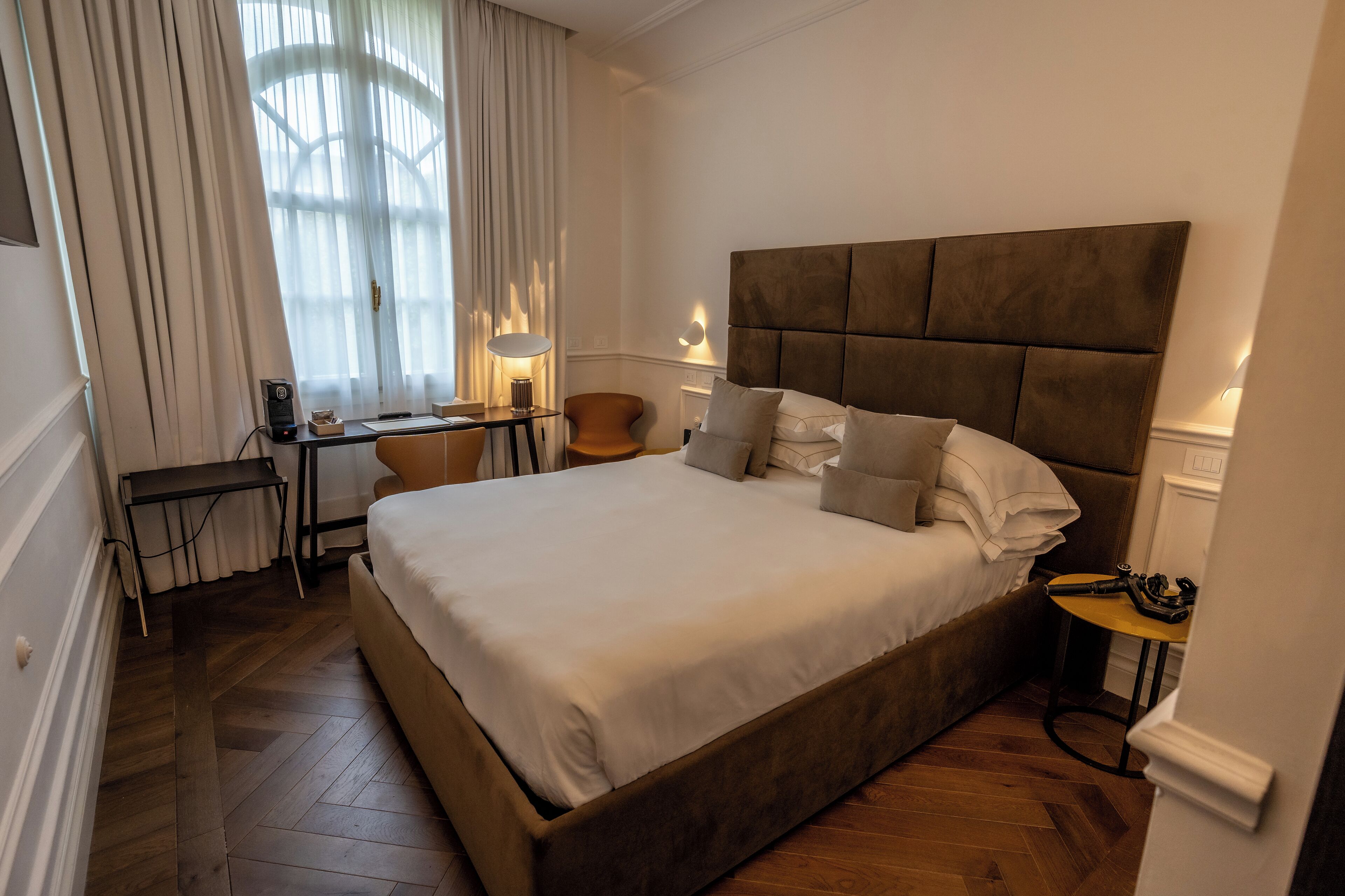 A hotel room with a large bed, a desk with a lamp, a chair, and a small table with a phone.