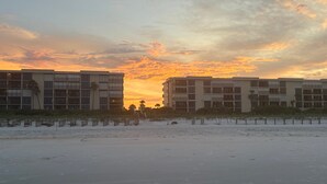 A beachfront hotel with multiple floors, a sandy beach in the foreground, and a sunset sky. - Sand Dollar 2-201 Direct Oceanfront Corner Unit (Saint Augustine)