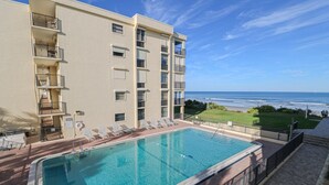 A swimming pool with lounge chairs, a view of the ocean, and a building with balconies. - Sand Dollar 2-201 Direct Oceanfront Corner Unit (Saint Augustine)