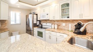 A kitchen with white cabinets, a stainless steel refrigerator, a microwave, an oven, a coffee maker, and a granite countertop.