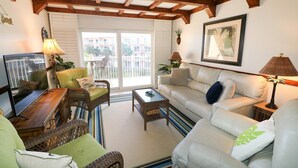 Un salon comprenant un canapé, des fauteuils, une table basse, un téléviseur et un balcon offrant une vue sur les immebles.