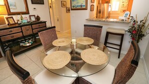 Un coin repas avec une table ronde en verre, des chaises en osier et une cuisine en arrière-plan.