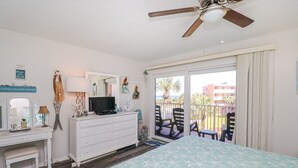 Une chambre à coucher comprenant un lit, une commode, une télévision et un balcon avec des chaises.