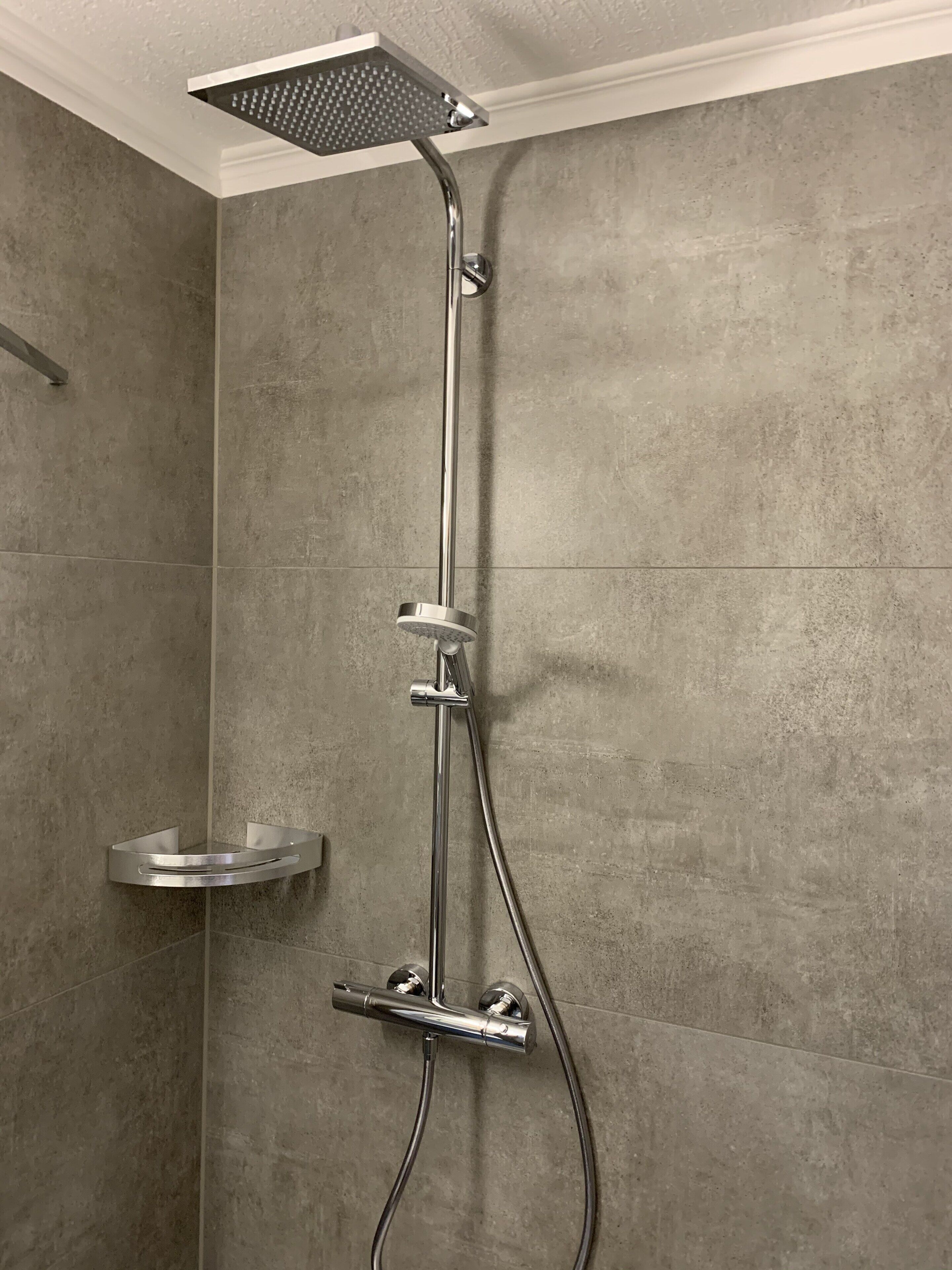 A shower with a square head, a handheld showerhead, and a handheld faucet.