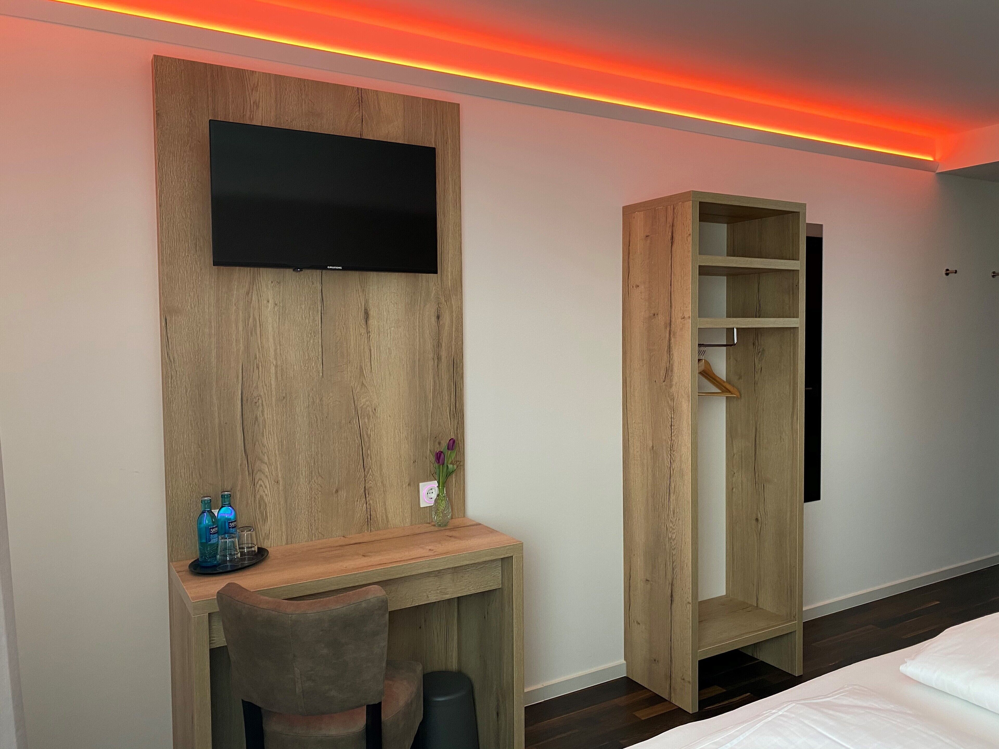 Una habitación de hotel moderna con un escritorio de madera, un televisor de pantalla plana, un armario y una cama.