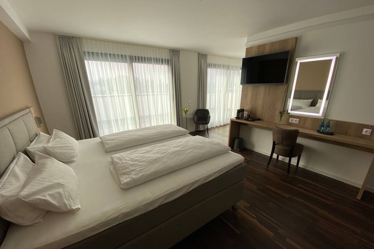 A hotel room with a large bed, a desk with a mirror, and a television.