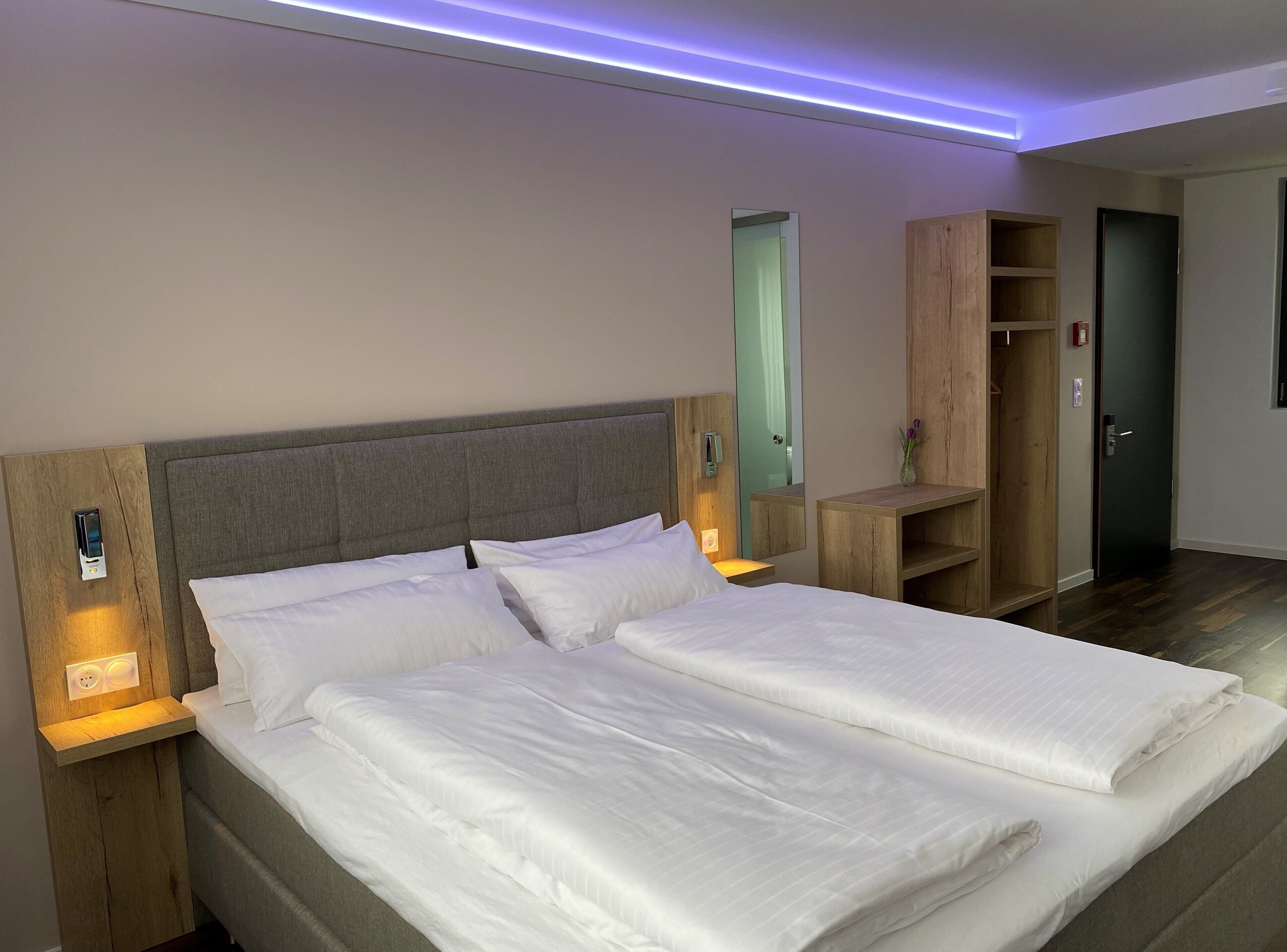 A double bed with a grey headboard, bedside tables with lamps, a wooden wardrobe, and a mirror.