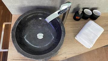 Un lavamanos de piedra negra con un grifo moderno, una bandeja de madera y una toalla blanca.
