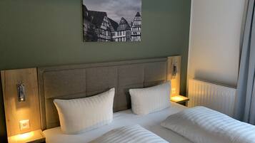 A hotel room with a large bed, two bedside tables, a headboard, and a painting of a European town on the wall.