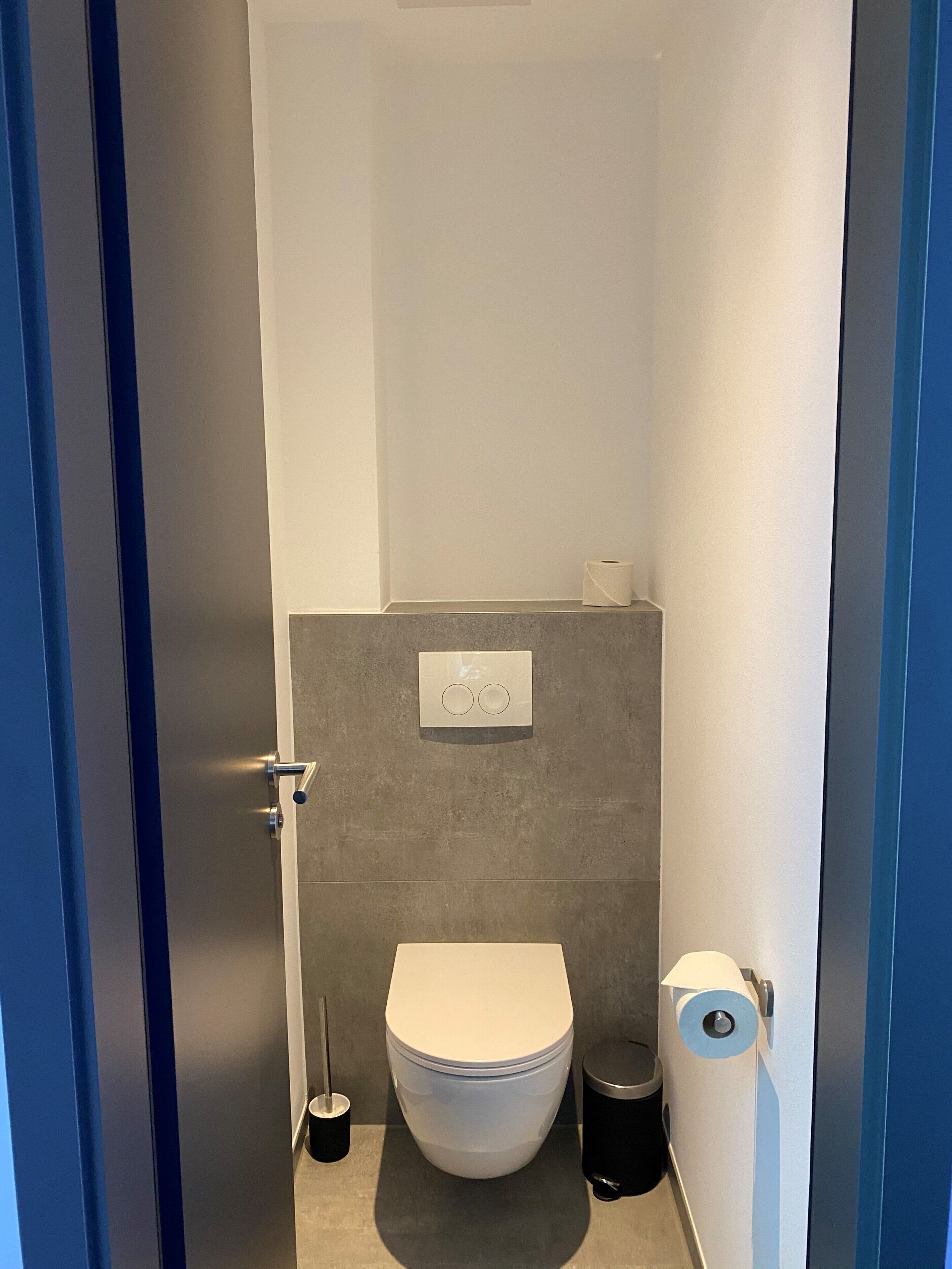A compact bathroom with a toilet, a trash bin, and a toilet paper holder.