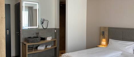 A modern hotel room with a large bed, a built-in vanity with a mirror, a hairdryer, and neatly folded towels.