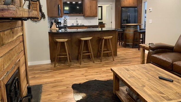 A modern kitchen with wooden cabinets, a central island with stools, a bar area, and a leather sofa in a living area. - Excellent location right across the street from the Expo Center! – Sleeps 8 (Tulsa)