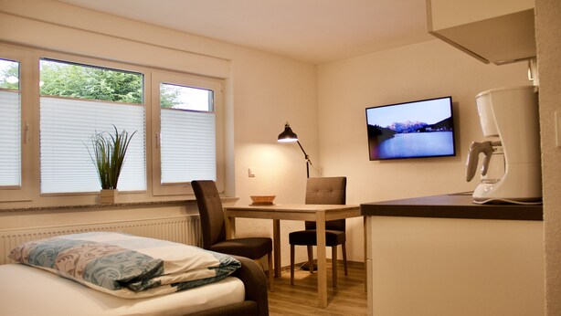 A compact room with a bed, a desk, a chair, a television, and a radiator.