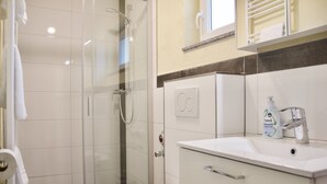 A modern bathroom with a glass-enclosed shower, a white sink with a soap dispenser, and a toilet.