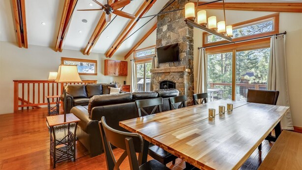 A spacious living area with a stone fireplace, wooden ceiling beams, and a large dining table. - Spacious Retreat at Dollar Point (Tahoe City)