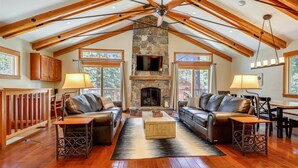 A spacious living room with a stone fireplace, leather sofas, wooden flooring, and a high ceiling with exposed beams. - Spacious Retreat at Dollar Point (Tahoe City)