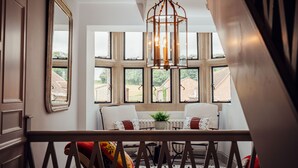 Una habitación con un amplio ventanal, una silla blanca, una mesa con una planta y una lámpara colgante.