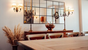 Un comedor con un espejo rectangular grande, apliques de pared, un cuenco de cobre y un jarrón de plumas de hierba de pampa.