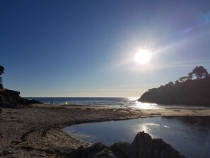 Ein Strand mit felsigem Ufer, ruhigem Wasser und blauem Himmel.