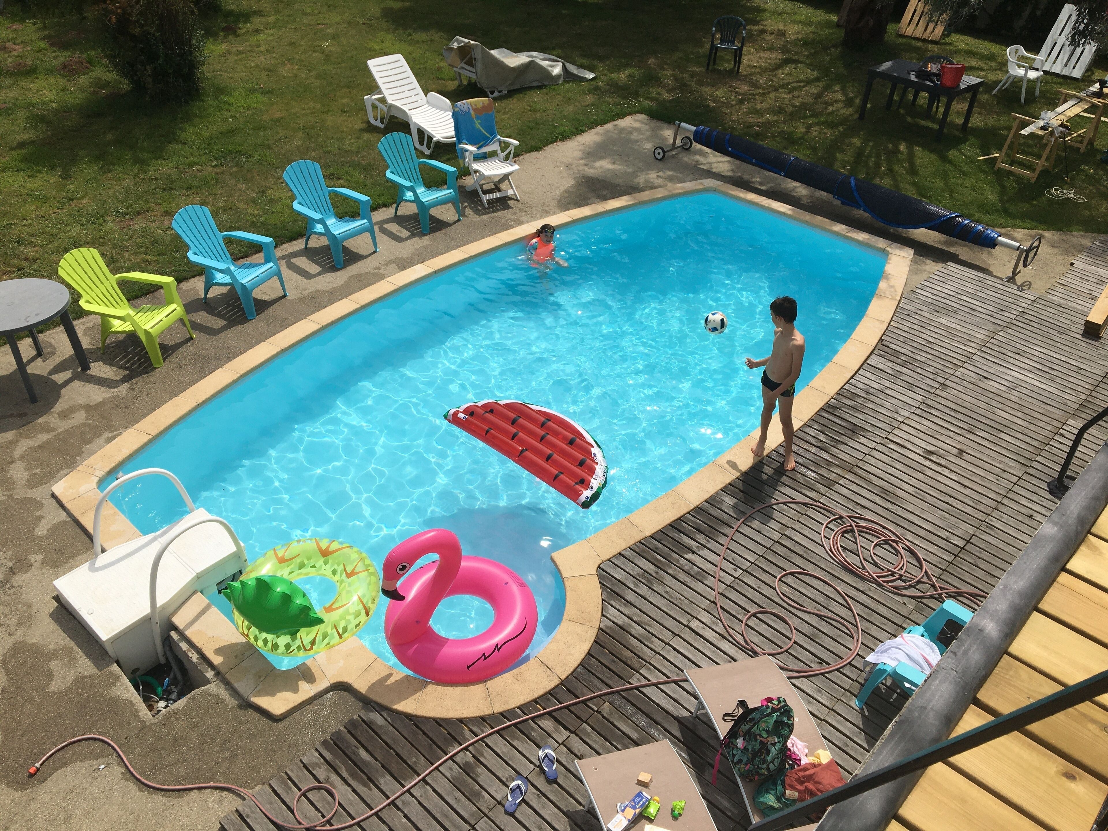 A rectangular swimming pool with a wooden deck surrounding it, featuring lounge chairs and inflatable toys.