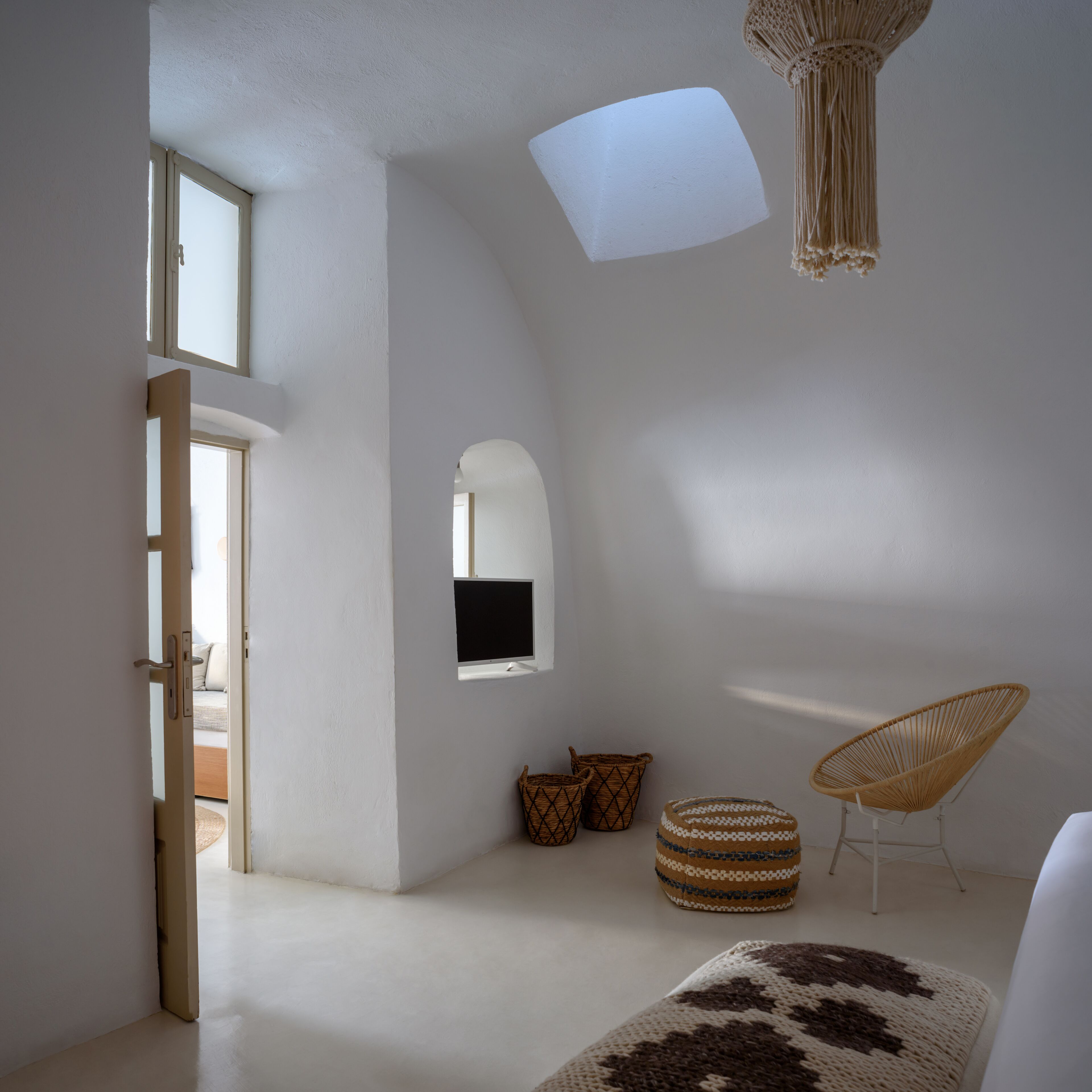 A modern, minimalist room with a large window, a flat-screen TV, a woven chair, and a patterned rug.