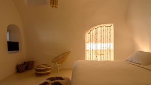 A bedroom with a bed, a chair, and a window with curtains. - Suite Home Santorini (Santorini)