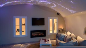 A cozy living room with a fireplace, a flat-screen TV, and a sofa with cushions. - Suite Home Santorini (Santorini)