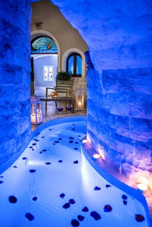 Ein Innenpool mit blauer Beleuchtung, Steinwänden und einer Sitzecke mit Tisch und Stühlen.